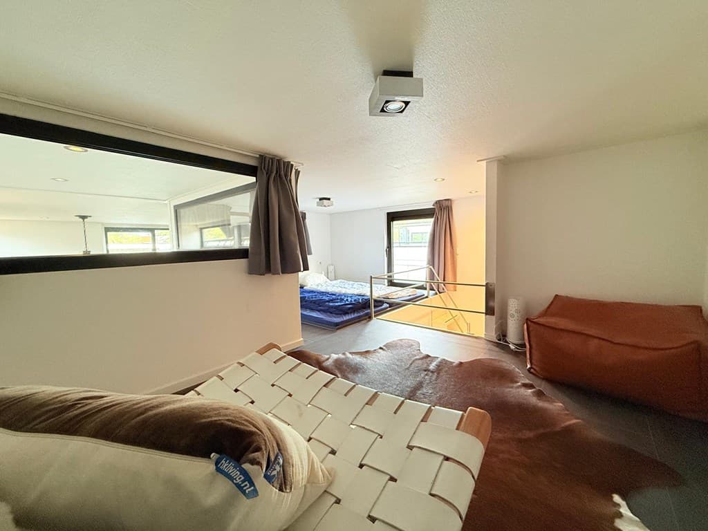 Slaapruimte met houten vloer, bed met blauw dekbed en bank, voorzien van natuurlijk licht en moderne aankleding.