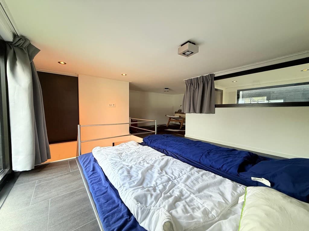 Een slaapkamer met twee bedden, grote ramen, meubels en een moderne uitstraling