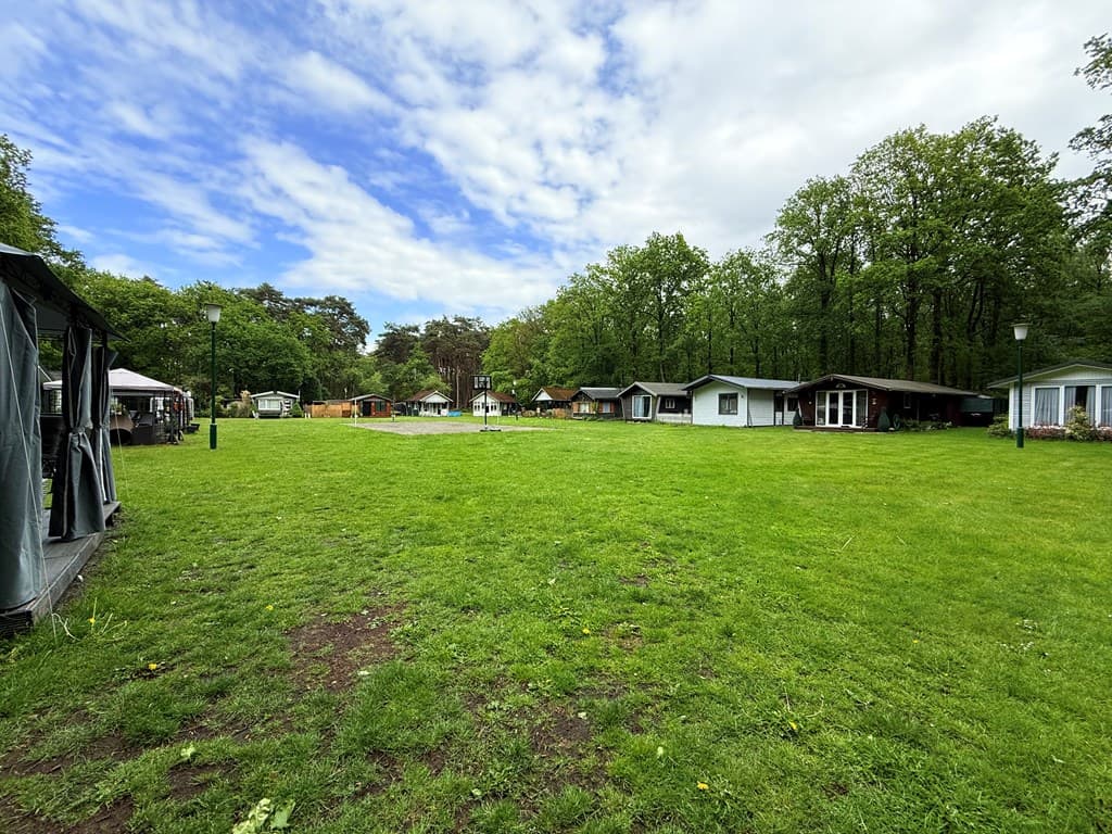 Groen grasveld met verschillende vakantiehuisjes en bomen op de achtergrond, onder een kleurrijke lucht