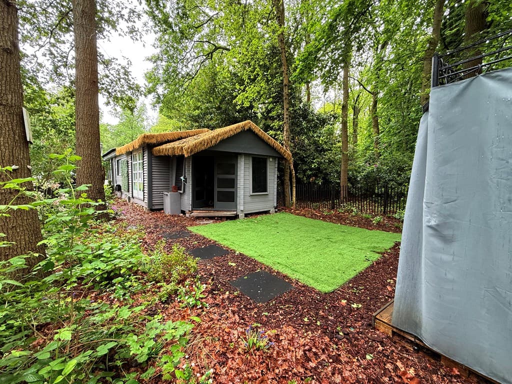 Vakantiewoning met rieten dak, gelegen in een bosrijke omgeving met groene grasmat en looppad.