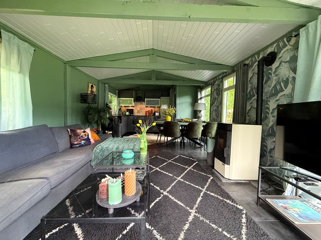 Woonkamer met groene wanden, zithoek, eettafel en een uitzicht op de keuken, lichte gordijnen en planten decoraties