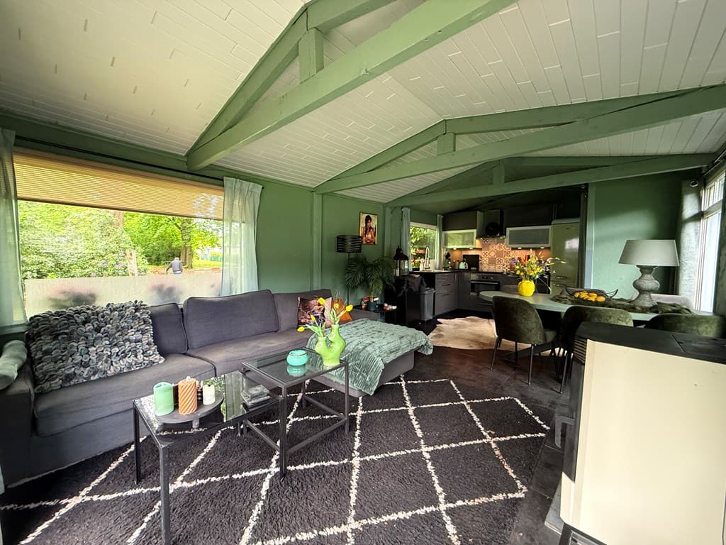 Woonkamer met groene muren, bank, moderne keuken en grote ramen met uitzicht op de tuin