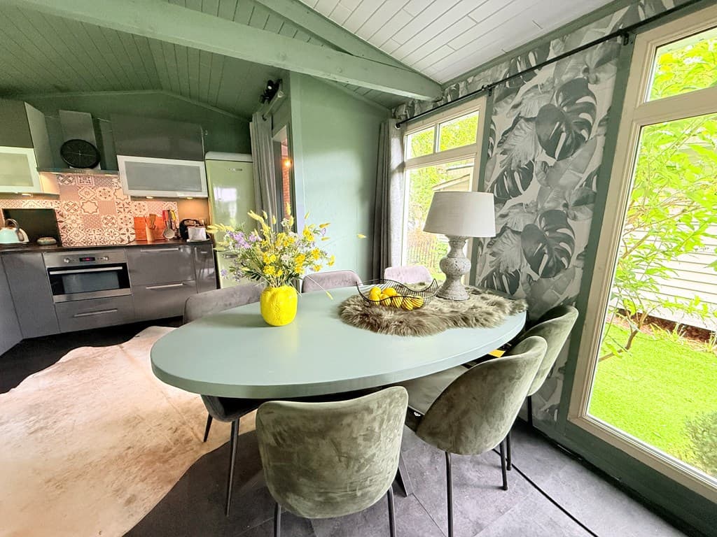 Licht en moderne eetruimte met een ovale tafel, stoelen, decoratieve lamp en grote ramen met uitzicht op de tuin.