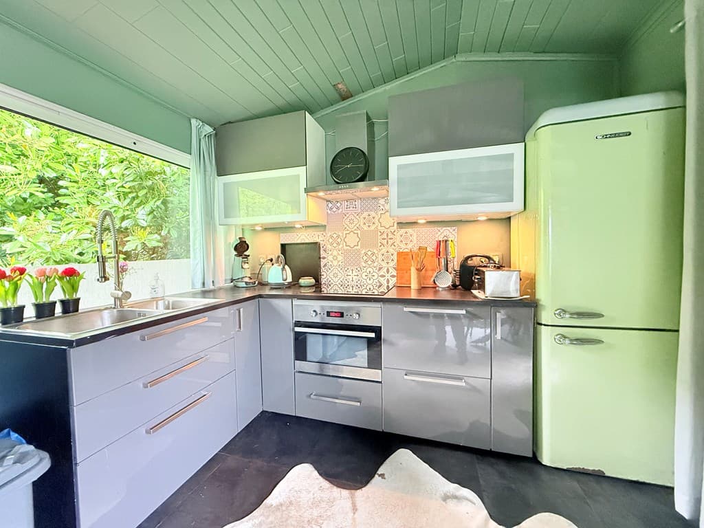 Moderne keuken met groene accenten, roestvrijstalen apparatuur en een retro koelkast, verlicht door natuurlijk licht.