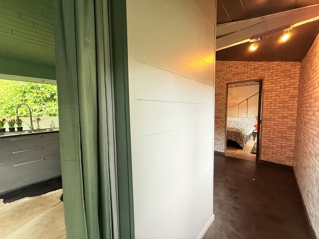 Interieur van een woning met een zicht op een gang, keuken aan de linkerkant en een slaapkamer met bakstenen muur aan de rech