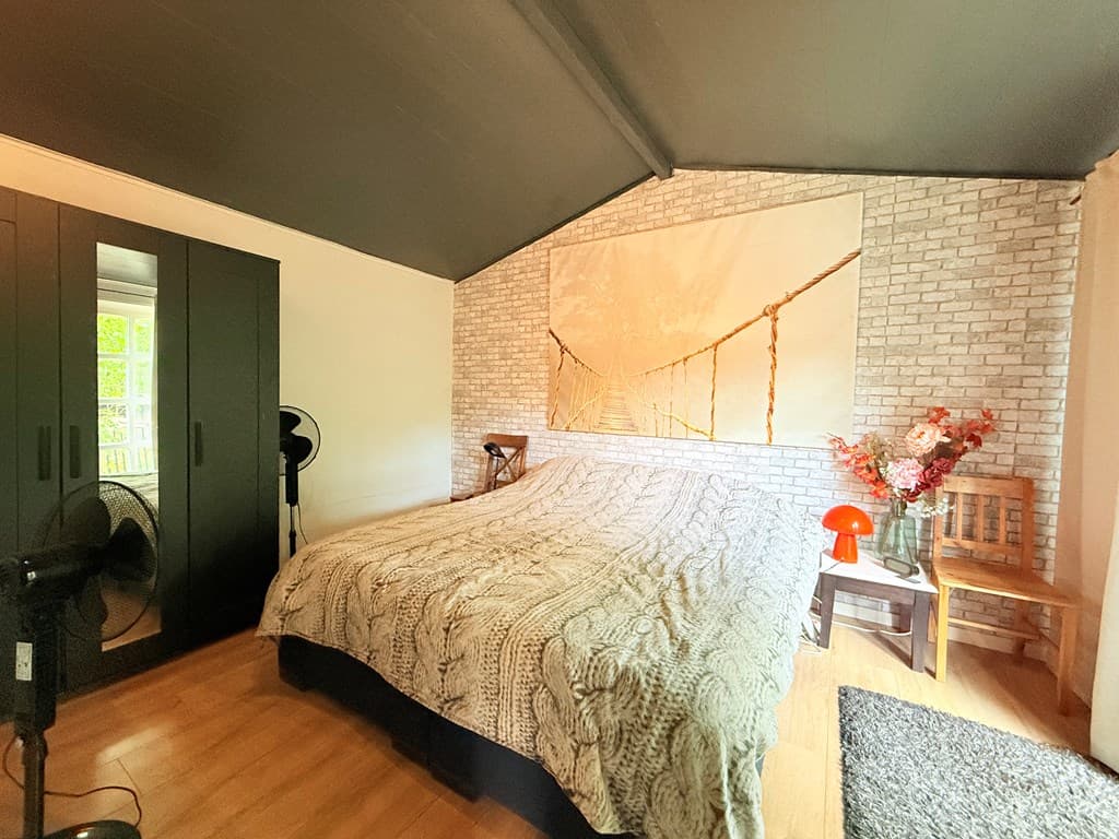 Slaapkamer met groot bed, zwart kast, wanddecoratie en zachte verlichting, houten vloeren en een stoel met een tafel