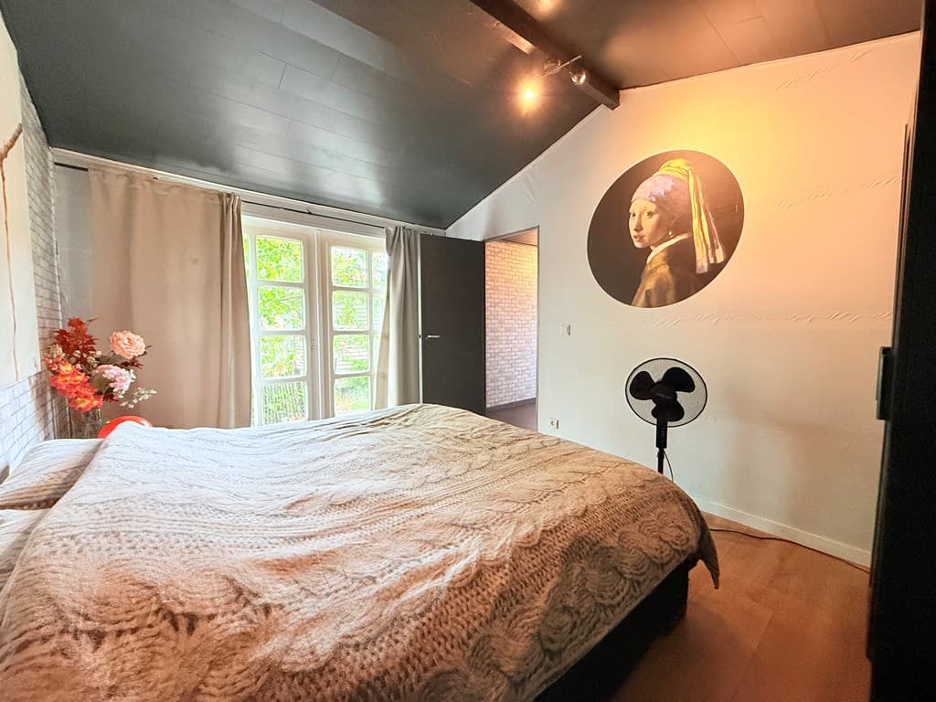 Sfeervolle slaapkamer met groot bed, kunst aan de wand en openslaande deuren naar buiten.