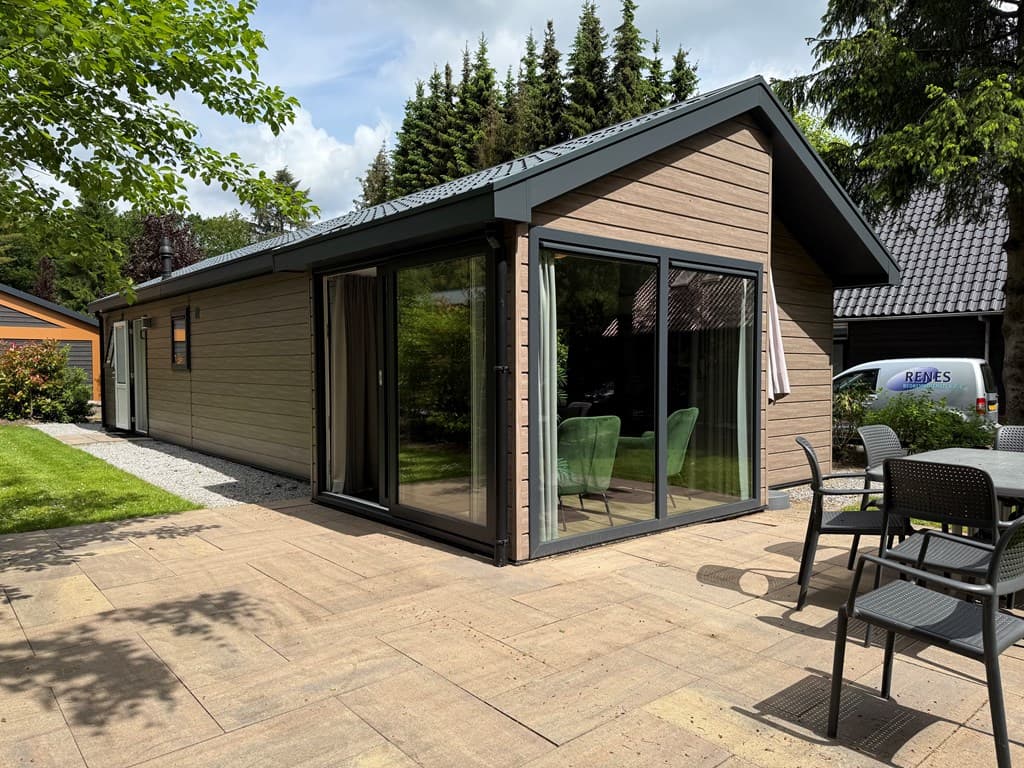 Moderne vakantiewoning met grote glazen schuifdeuren, een patio en groene planten rondom op EuroParcs Resort De Utrechtse Heu