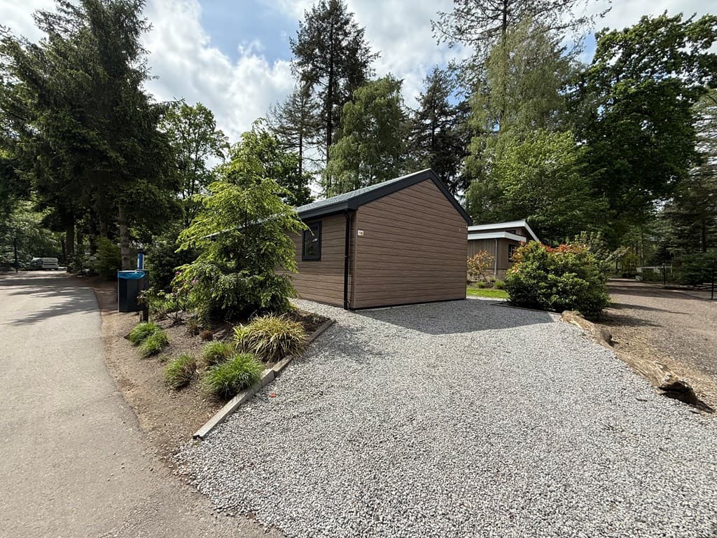 Houten vakantiewoning met een grindpad en groen begroeiing, gelegen in een bosrijke omgeving op EuroParcs Resort De Utrechtse