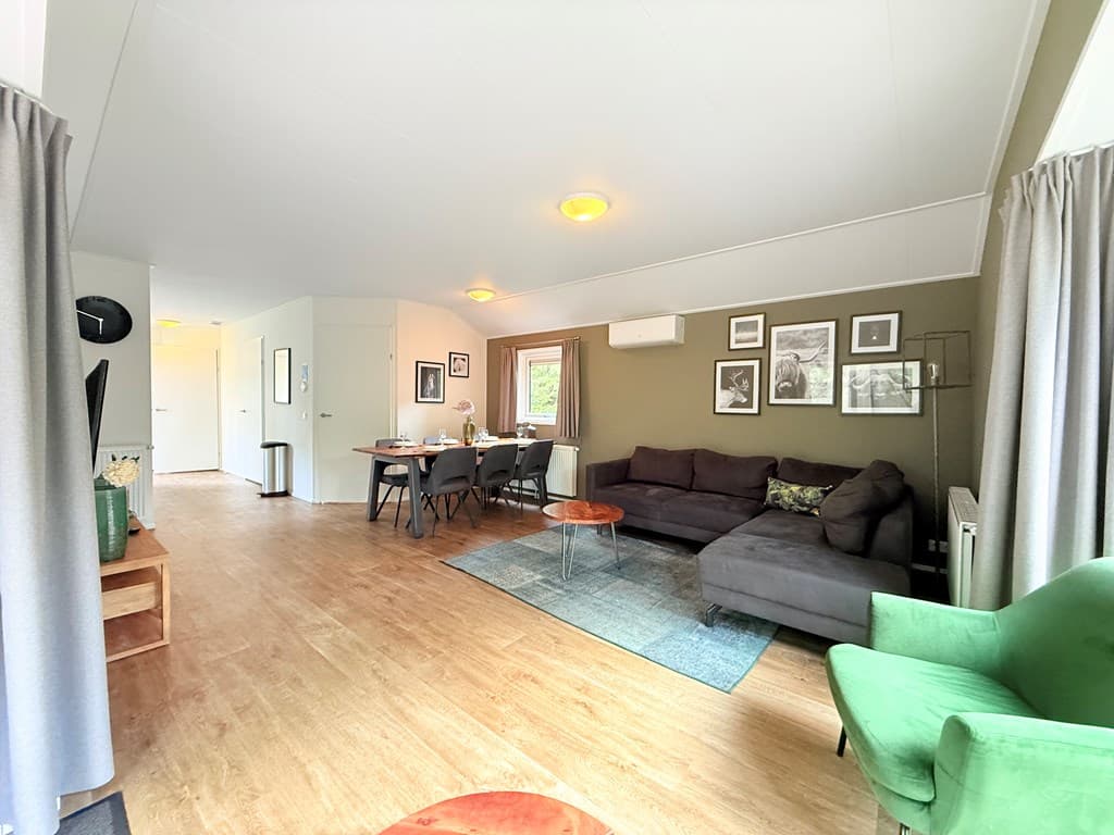 Ruime woonkamer met zithoek, eettafel en groene fauteuil, groene wand en foto's aan de muur in EuroParcs Resort De Utrechtse