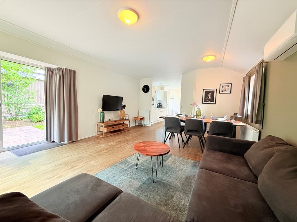 Woonkamer met zithoek, eettafel en toegang tot een terras met groene omgeving en een lichte inrichting
