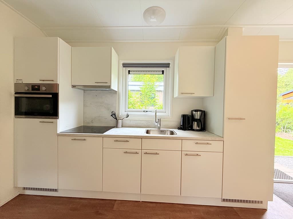 Moderne keuken met witte kasten, een spoelbak, kookplaat, oven en koffiezetapparaat zichtbaar aan de muur.