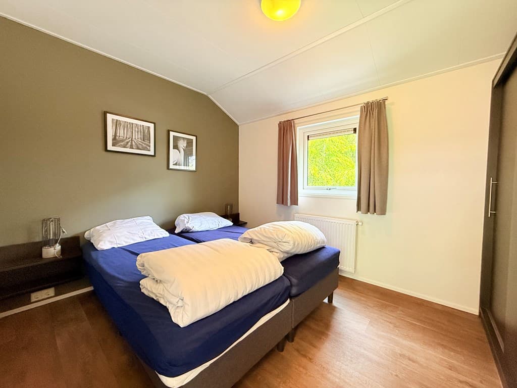 Slaapkamer met twee eenpersoonsbedden, houten vloer en ramen met gordijnen en schilderijen aan de muur