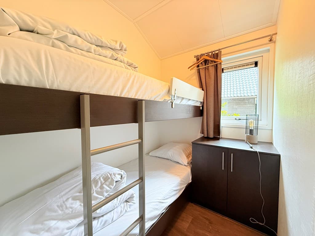 Slaapkamer met een stapelbed, een eenpersoonsbed en een kast onder een raam met een gordijn.