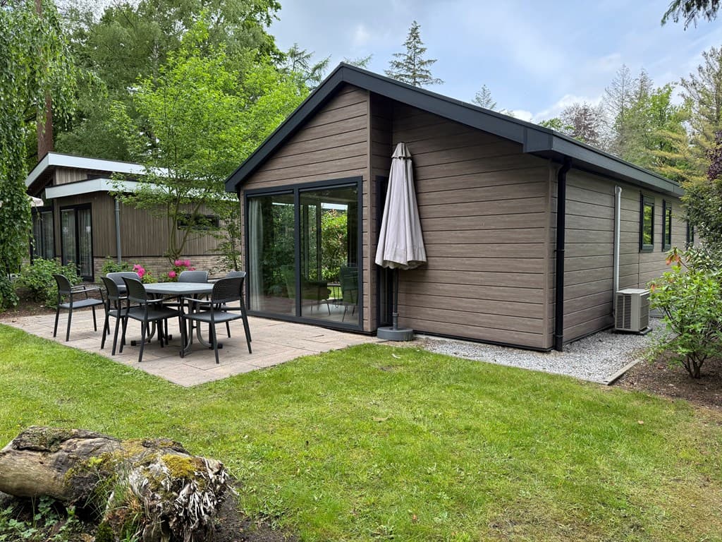 Moderne vakantiewoning met terras, tuinmeubilair en een parasol, omgeven door groen op EuroParcs Resort De Utrechtse Heuvelru