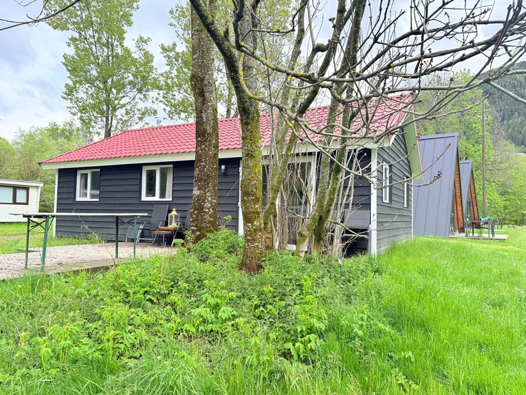 Houten woning met rode dak, omgeven door een grote groene tuin en meerdere bomen.