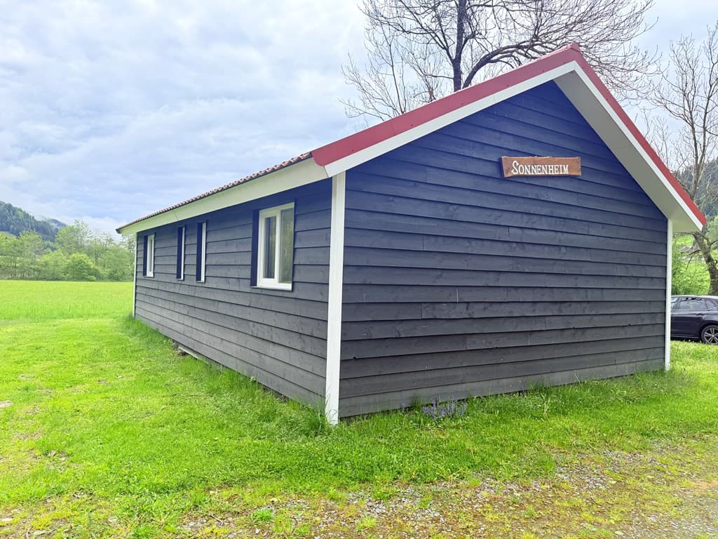 Zijaanzicht van een houten vakantiewoning met een rode dakrand en een bord met de naam Sonnleiten aan de gevel