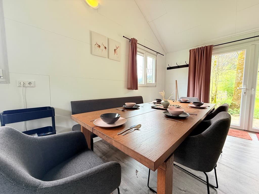 Eetkamer met houten tafel, stoelen en een groot raam met uitzicht op de tuin buiten.