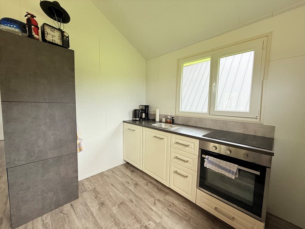 Keuken met moderne kasten, oven, aanrecht en raam met uitzicht op buiten.