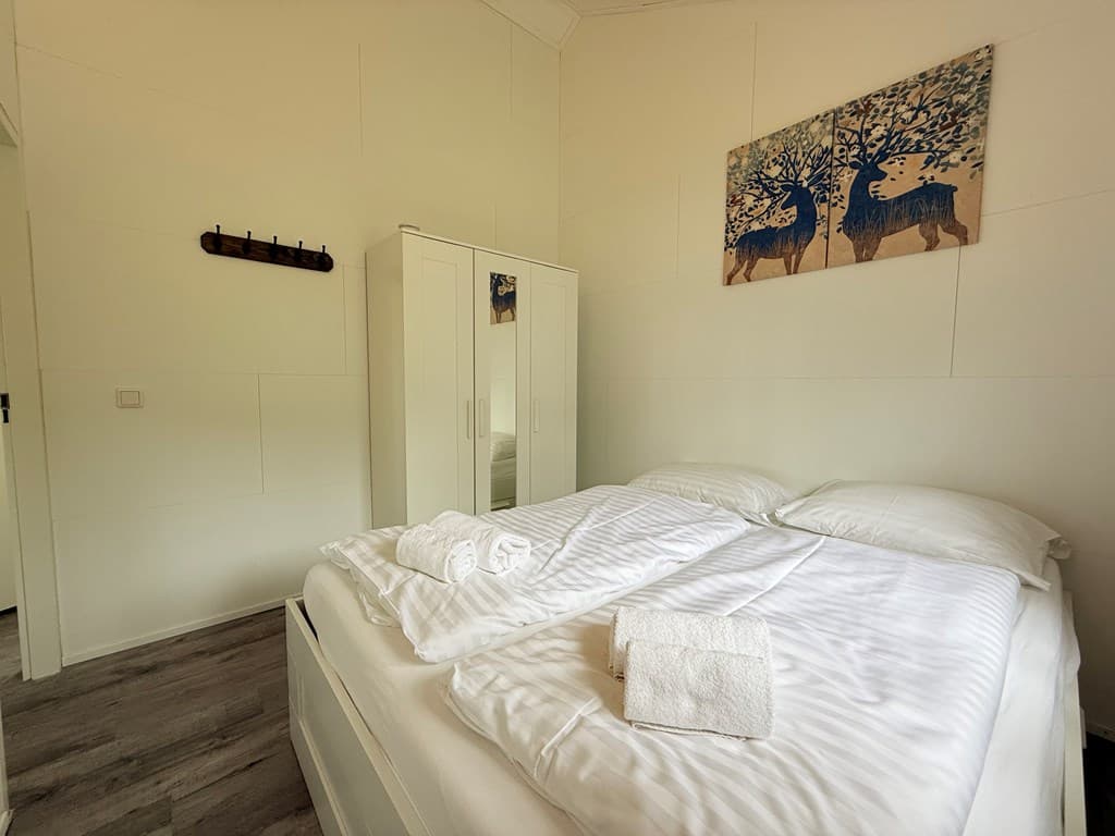 Slaapkamer met twee eenpersoonsbedden, witte linnen, kast en schilderij aan de muur.