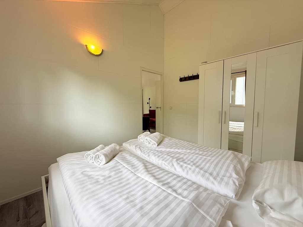 Hoofdslaapkamer met tweepersoonsbed, witte beddengoed en kasten in een lichte, neutrale ruimte