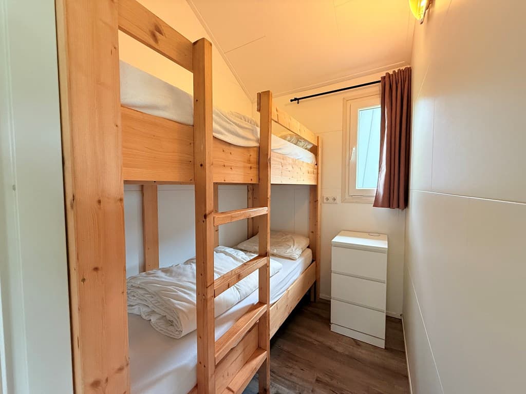 Slaapkamer met stapelbed en een wit nachtkastje naast een raam met gordijnen.