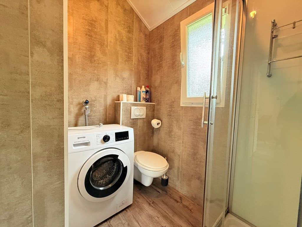 Badkamer met douche, toilet, wasmachine en wandplank met toiletartikelen in een moderne afwerking