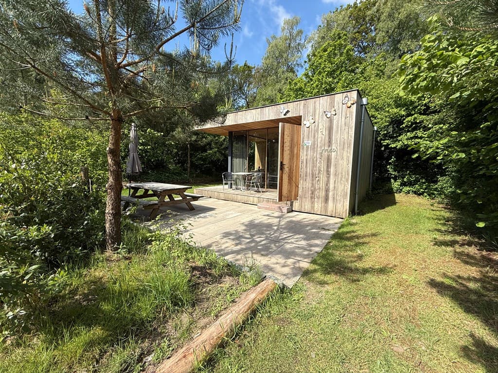 Houten vakantiehuisje met terras en tuin omringd door groen op EuroParcs De Wije Werelt in Otterlo