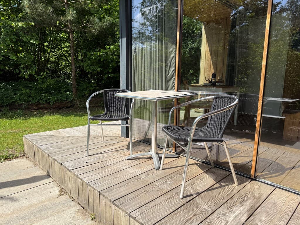 Terras met twee zwarte stoelen en een tafel, omringd door groen en met een groot glazen schuifdeur naar binnen.