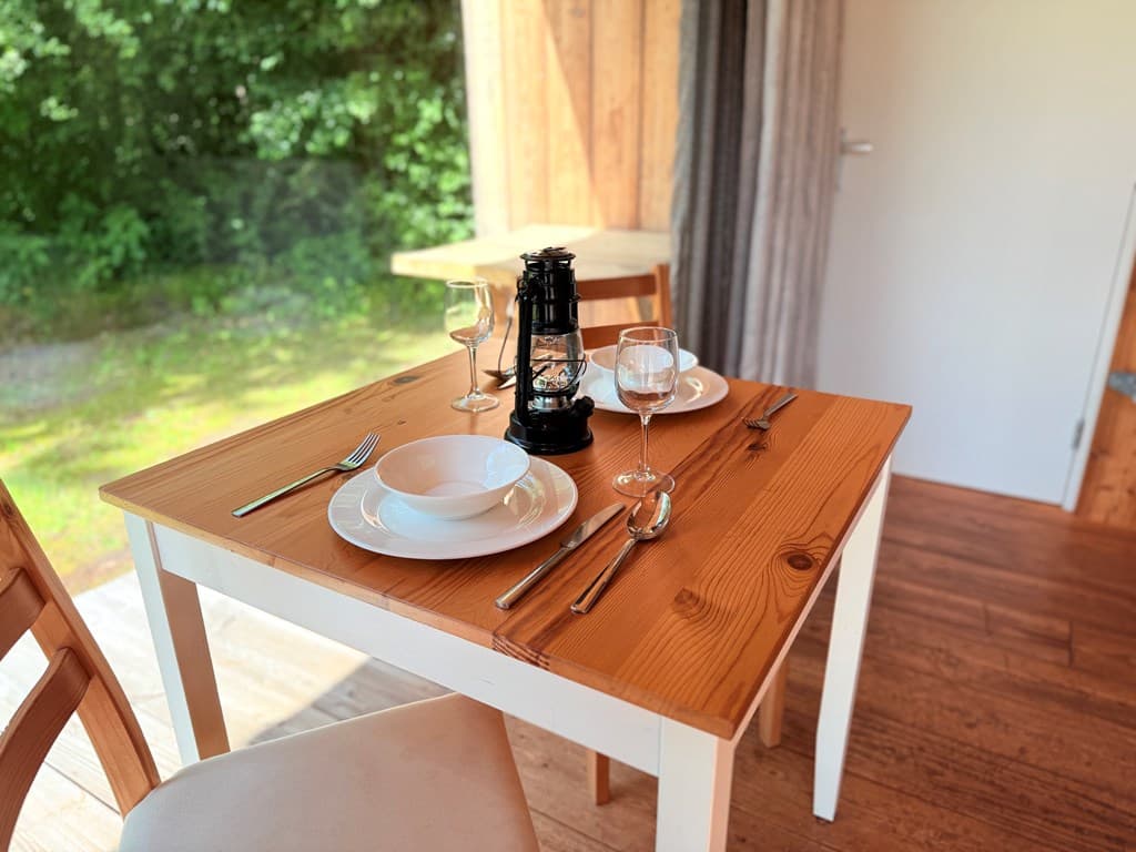 Eettafel met borden, bestek en een lantaarn, omgeven door groene natuur en lichtinval van buiten.