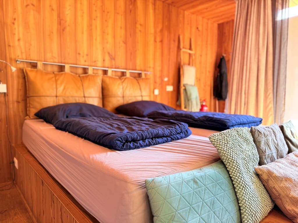 Sfeervolle slaapkamer met houten wanden, twee aparte bedden en verschillende kussens in pastelkleuren.