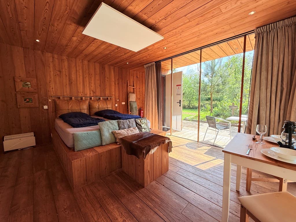 Gezellige slaapkamer met houten wanden, twee eenpersoonsbedden, toegang tot een terras en uitzicht op groene natuur.
