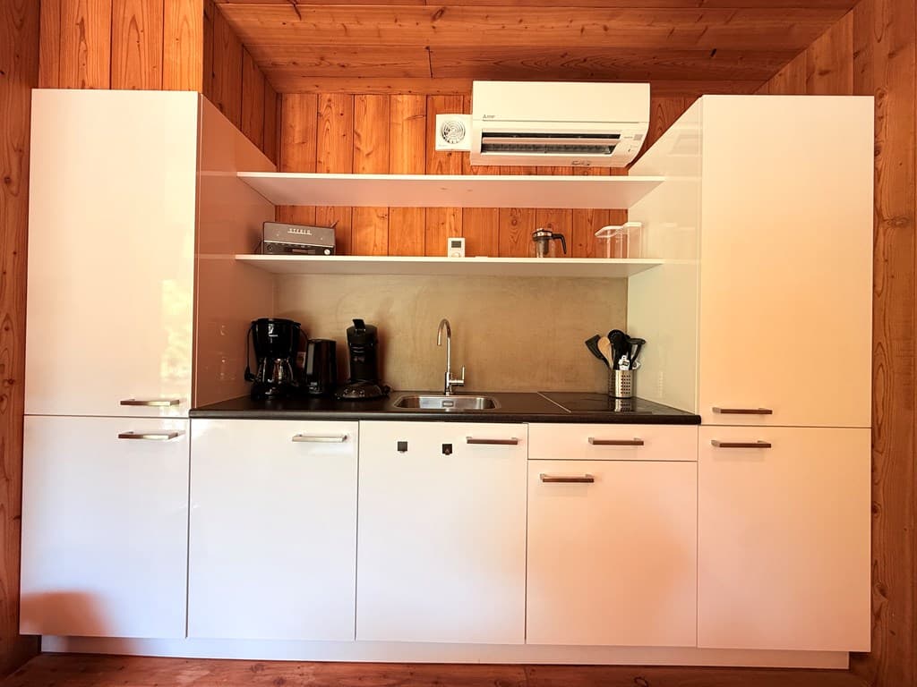 Moderne keuken met witte kastjes, aanrecht, waterkraan en diverse keukenapparatuur in houten ruimte.