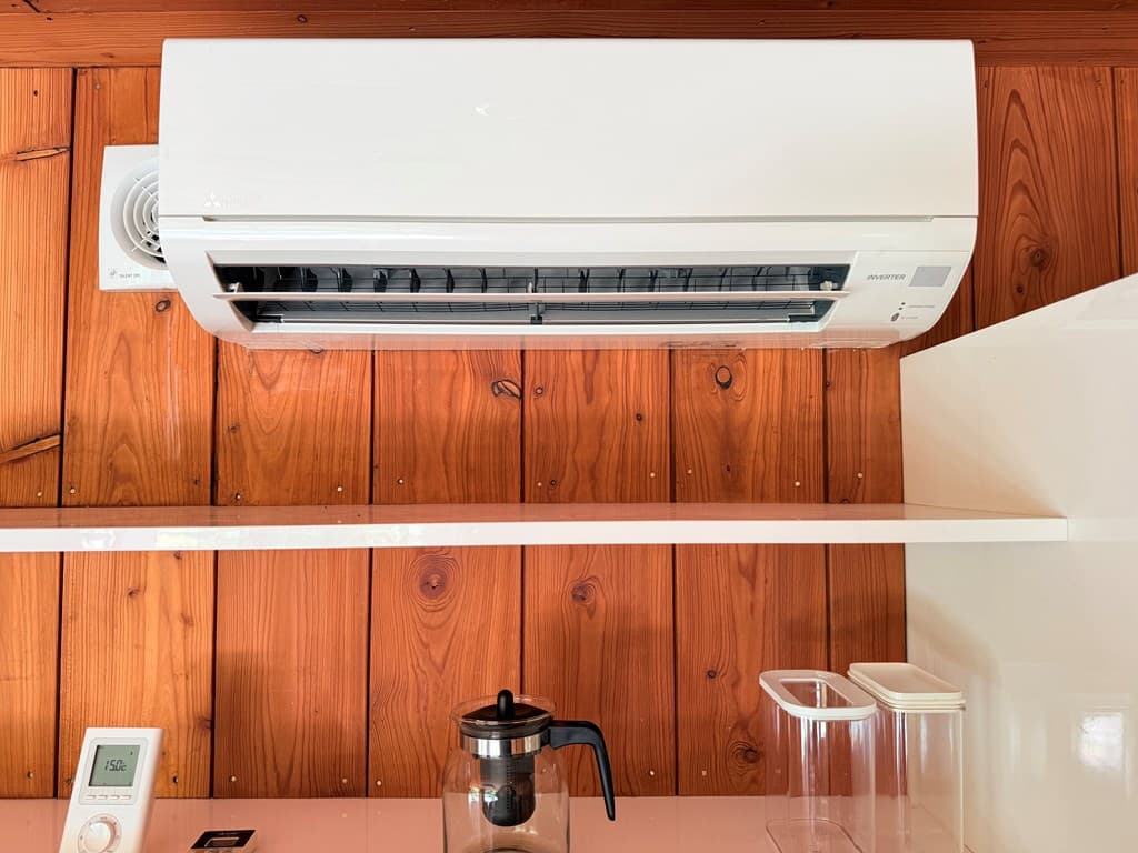 Witte airco boven een houten wand met een koffiezetapparaat en glazen opslagcontainers in een vakantiewoning