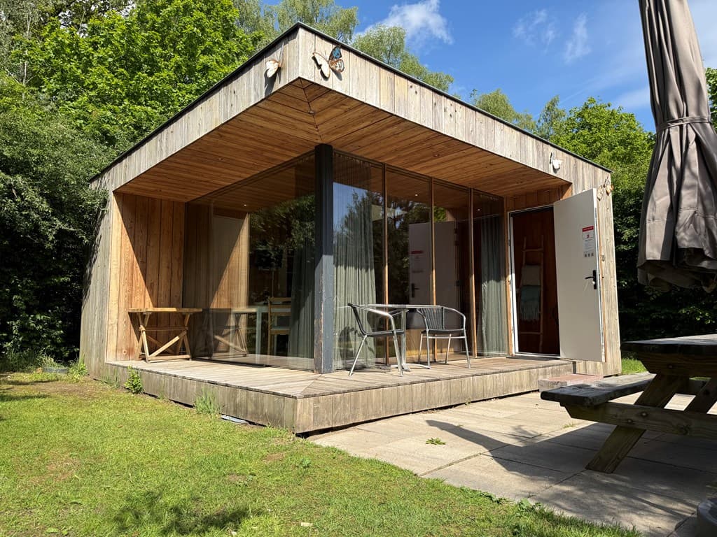 Moderne vakantiewoning met houten gevel, glazen schuifpui en terras met stoelen en tafel in een groene omgeving