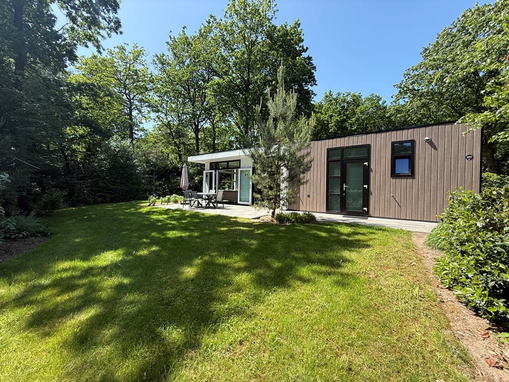 Moderne vakantiewoning met grote tuin, houten gevel en terras met zitgelegenheid, omringd door bomen