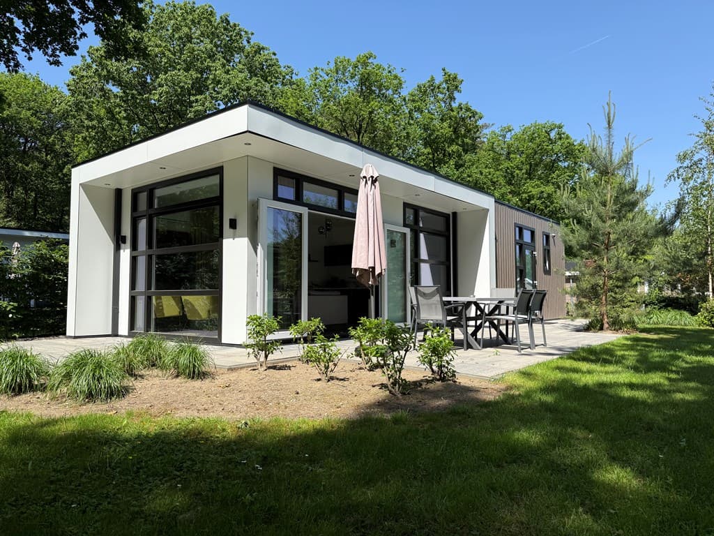 Moderne vakantiewoning met grote ramen en een terras, omgeven door groen en bomen op Recreatiepark Beekbergen