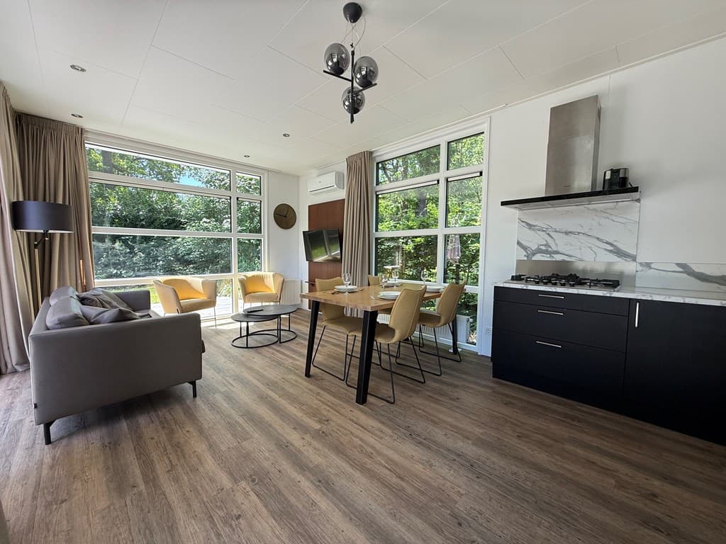 Moderne woonkamer met eetruimte, grote ramen en open keuken met gasfornuis en marmeren backsplash.