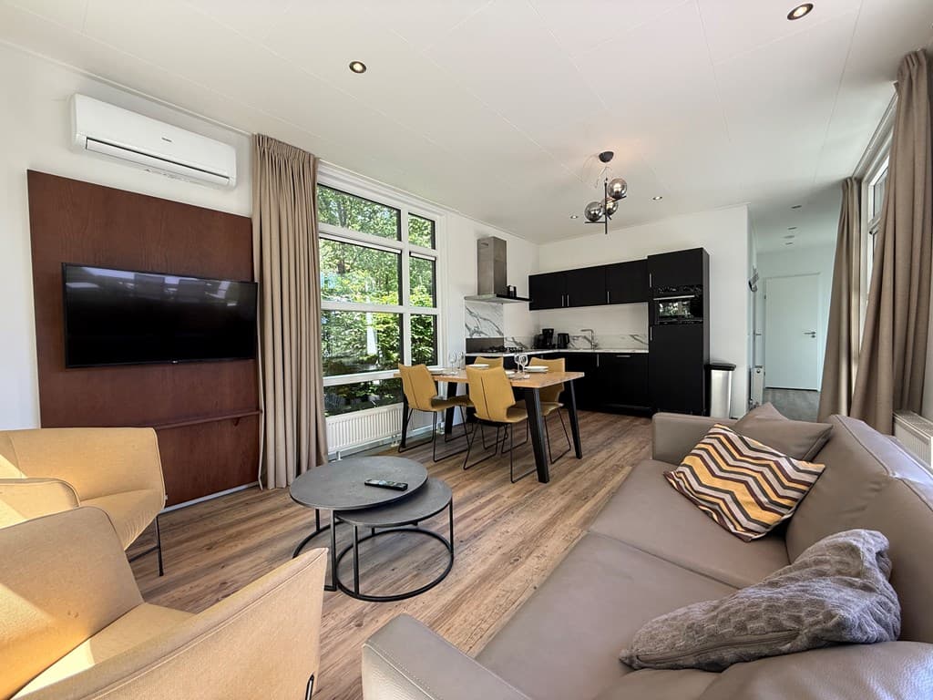 Modern woonkamer met eethoek, keuken en grote ramen, voorzien van comfortabele meubels en een tv.