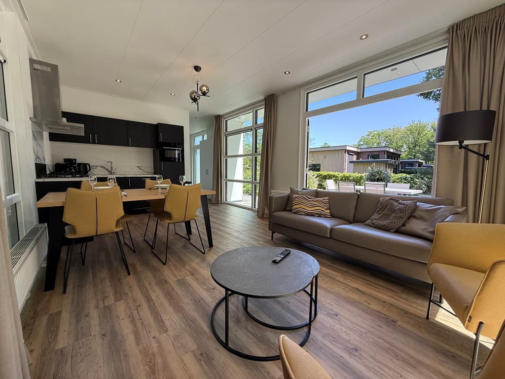 Moderne woonkamer met open keuken, eettafel en zitgedeelte, grote ramen en uitzicht op het terras buiten.