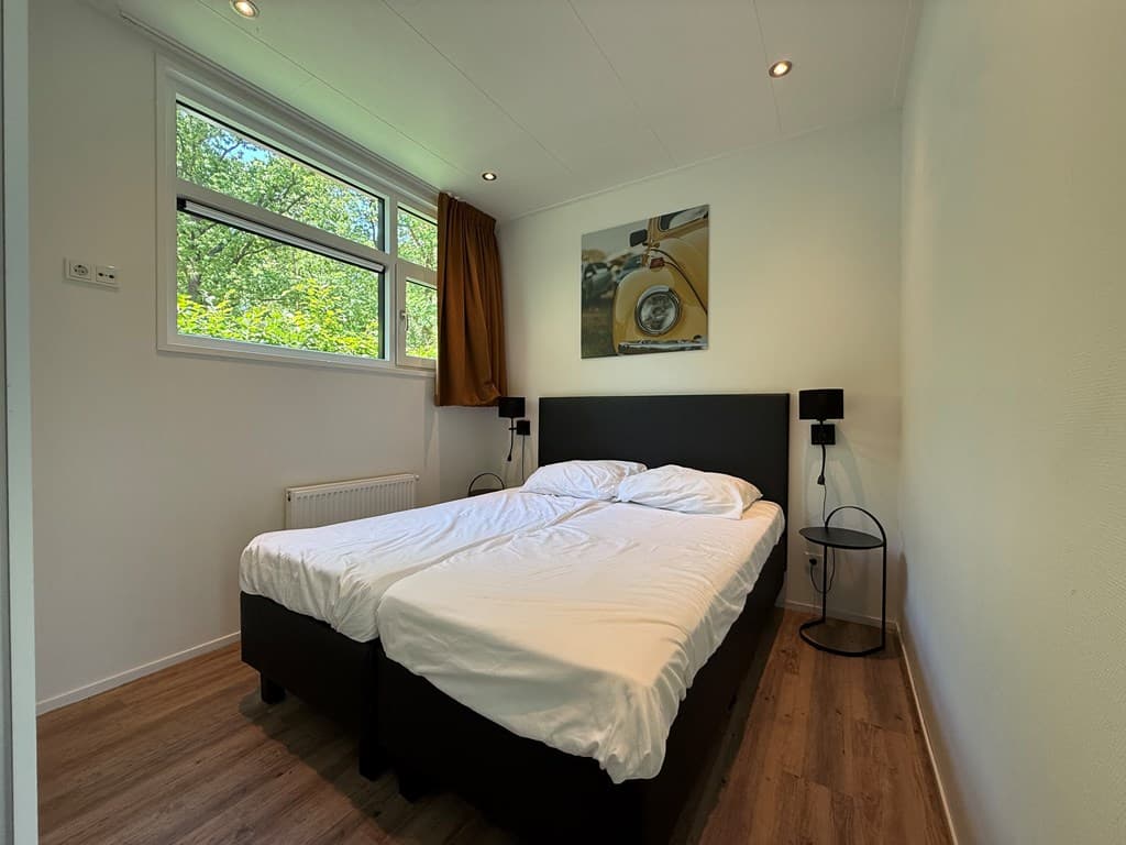 Slaapkamer met twee eenpersoonsbedden, nachtkastjes, raam met uitzicht op bomen en een schilderij aan de muur