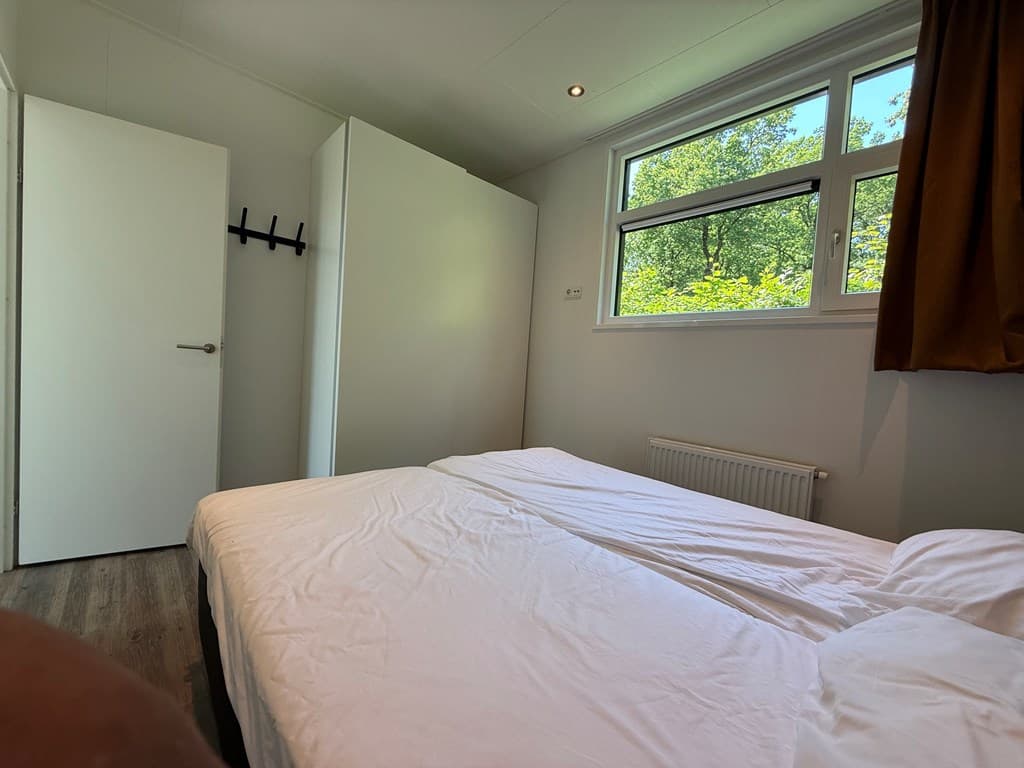 Slaapkamer met twee losse bedden, een grote kast en een raam met uitzicht op groene bomen.