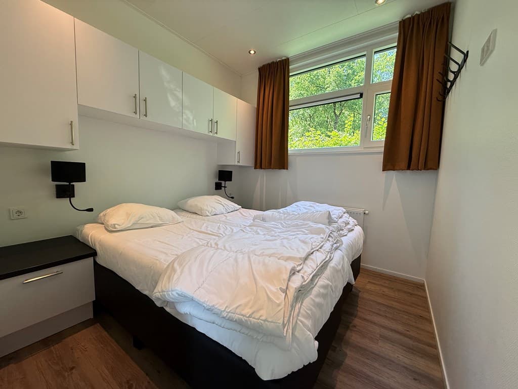 Slaapkamer met twee eenpersoonsbedden, witte beddengoed en gordijnen, raam met uitzicht op groen buiten.