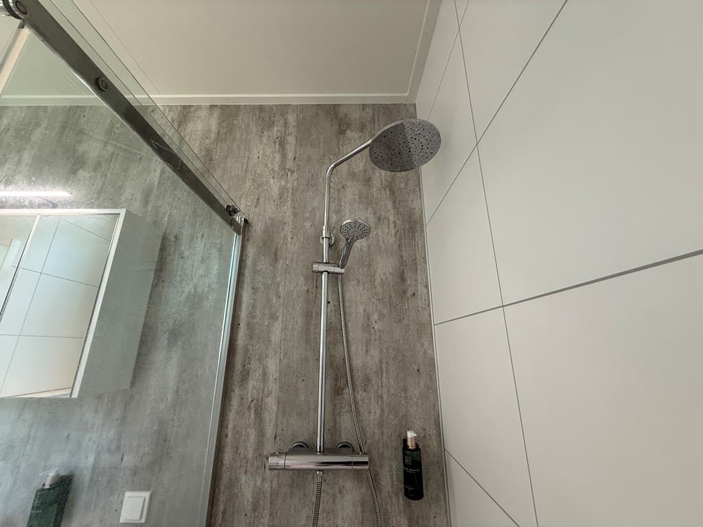 Inloopdouche met glazen wand, moderne regendouche en handdouche, omringd door lichte wandtegels en een houten vloer.