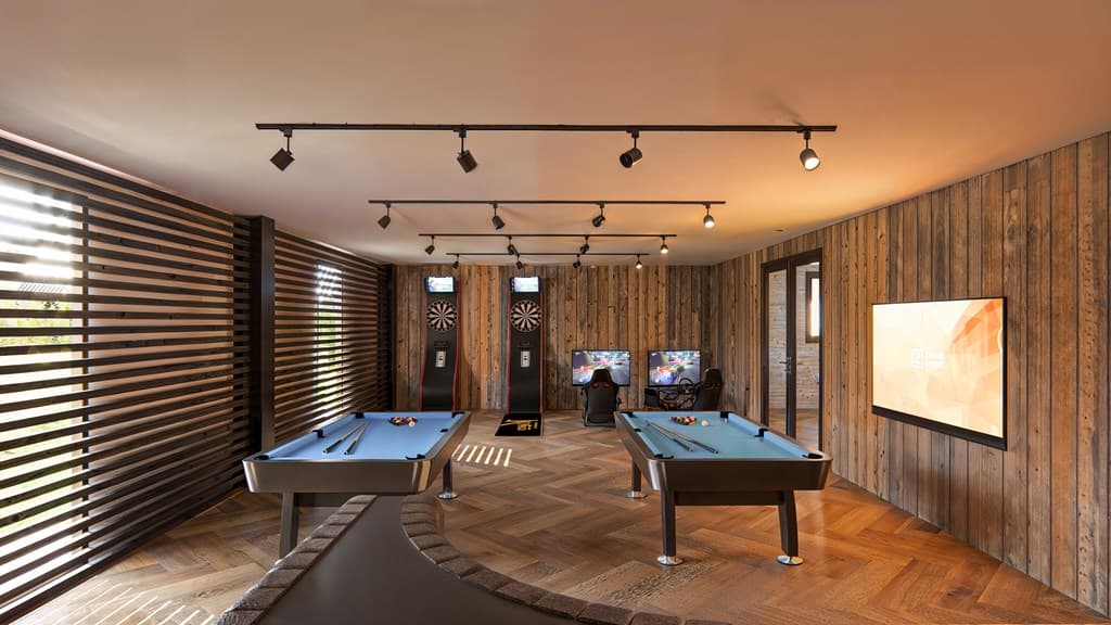 Spelletjesruimte met biljarttafels, dartborden en zithoek, afgewerkt met houten wanden en moderne verlichting
