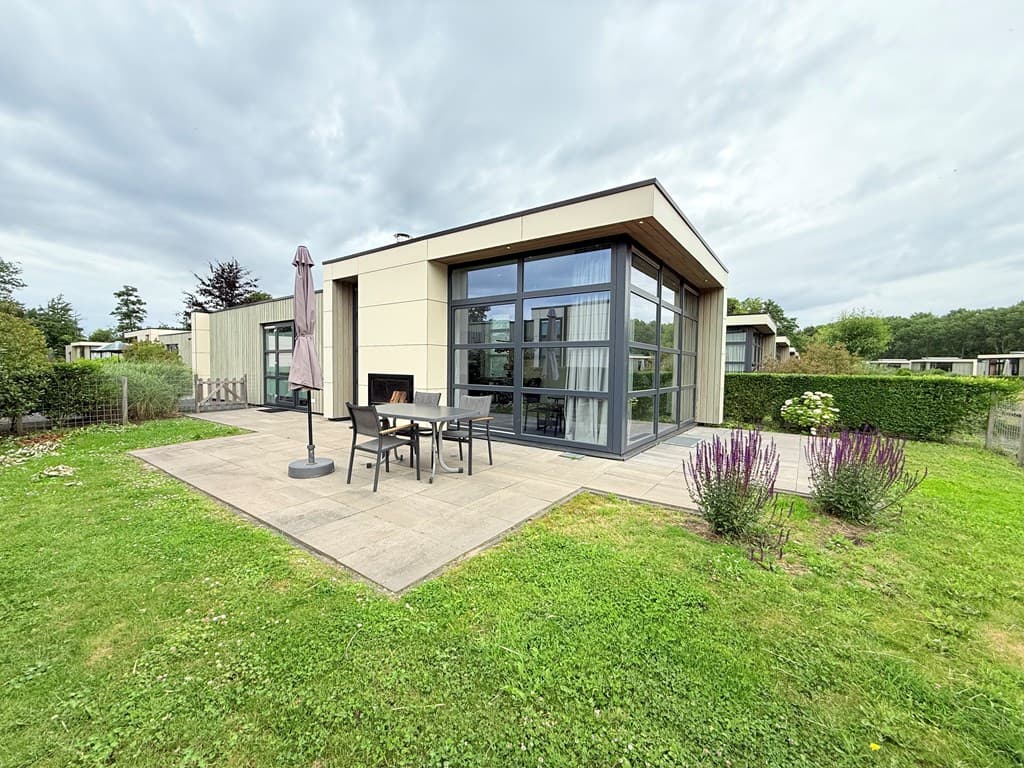 Moderne vakantiewoning met tuin, eetset en parasol, gelegen in een groene omgeving met gras en borders.
