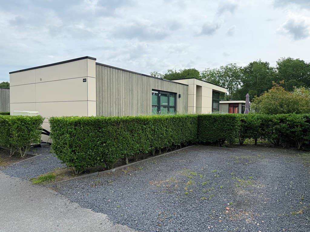 Moderne vakantiewoning met houten gevel en aangelegde tuin, gelegen tussen groene hagen en een grindpad