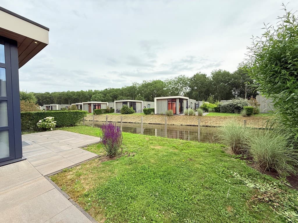 Uitzicht op vakantiewoningen aan het water met groen gras en struiken rondom in EuroParcs Buitenhuizen.