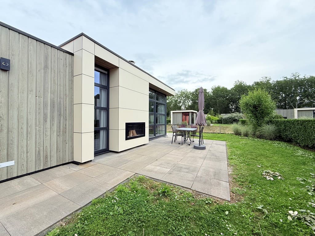 Moderne vakantiewoning met een terras, houten accenten en een groene tuin rondom de woning.
