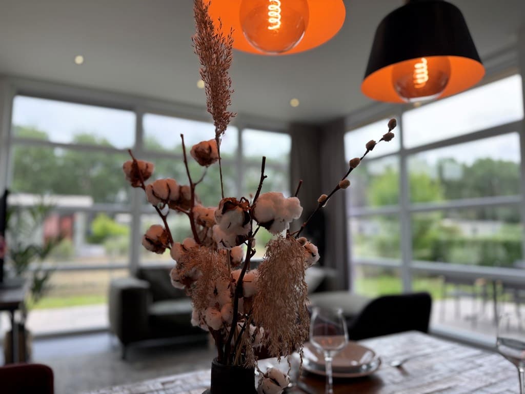 Interieur van een woning met een bloemenvaas en moderne lampen, grote ramen met uitzicht op het groen buiten